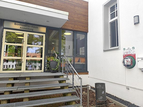 AED im Wandkasten, rechts an der Wand, neben der Treppe zum Eingang Bonhoeffer-Haus/Anmeldung